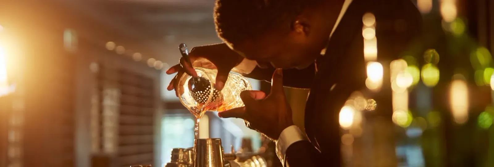 A bartender straining a cocktail under warm light at BAR 45