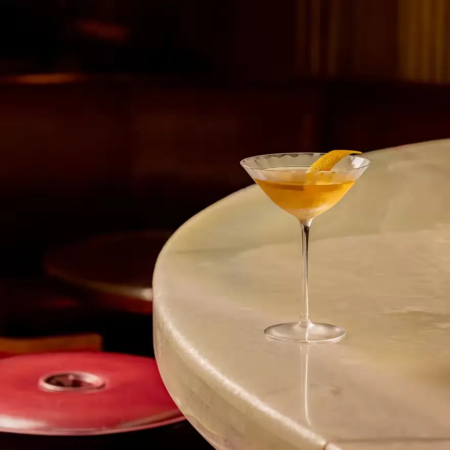 A pale amber cocktail with a lemon twist on the marble bar at Claridge's Bar
