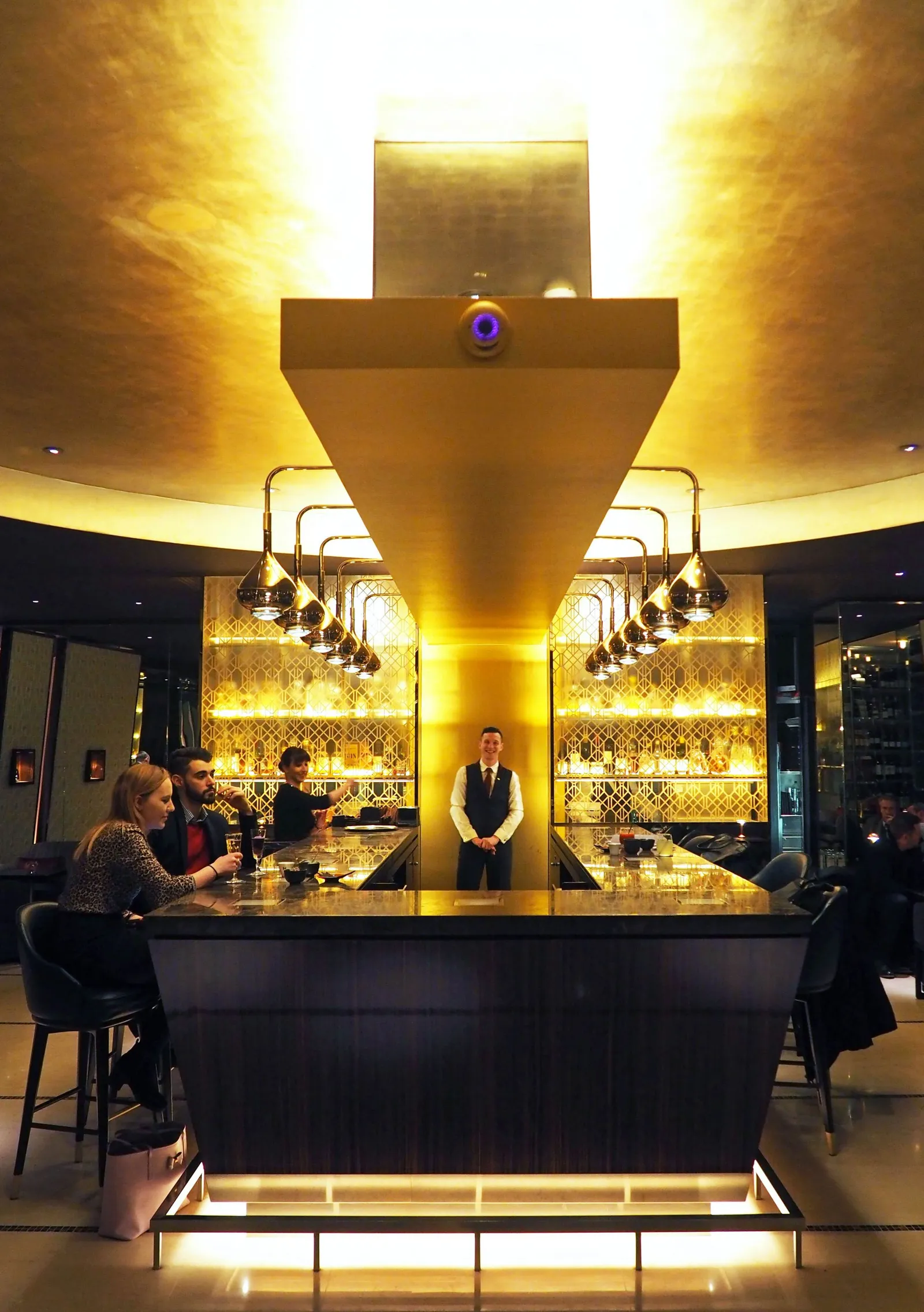 Guests seated around the central bar beneath suspended copper lights